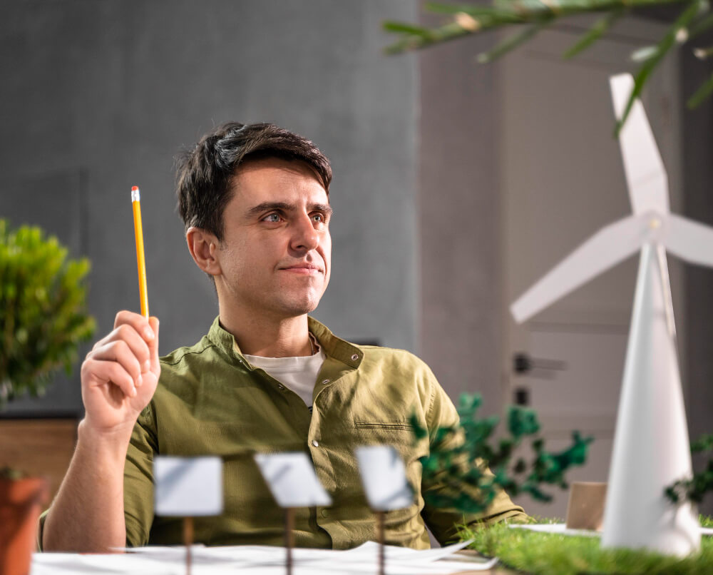 Homme tenant un crayon face à une maquette d'un environnement porté sur les énergies renouvelables.