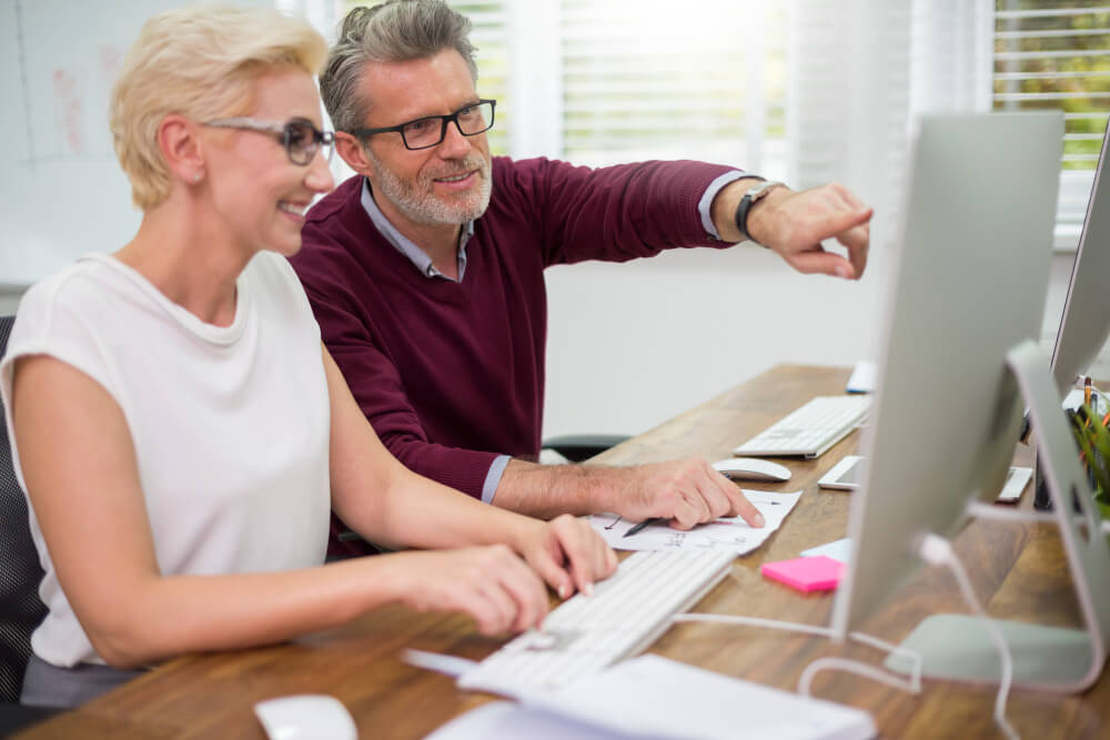 Deux seniors souriants devant un ordinateurs.